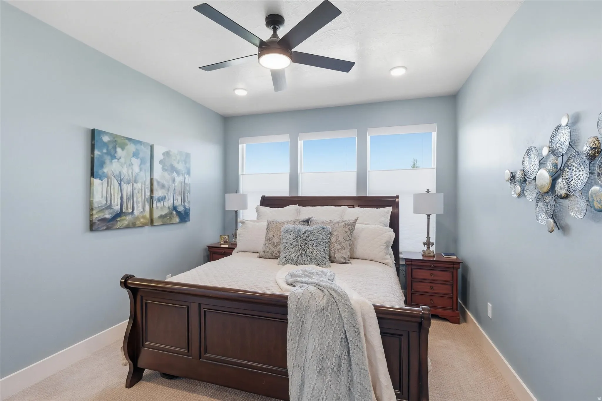Spacious bedroom featuring light blue walls, soft neutral carpet, a ceiling fan with integrated lighting, and three high-set windows