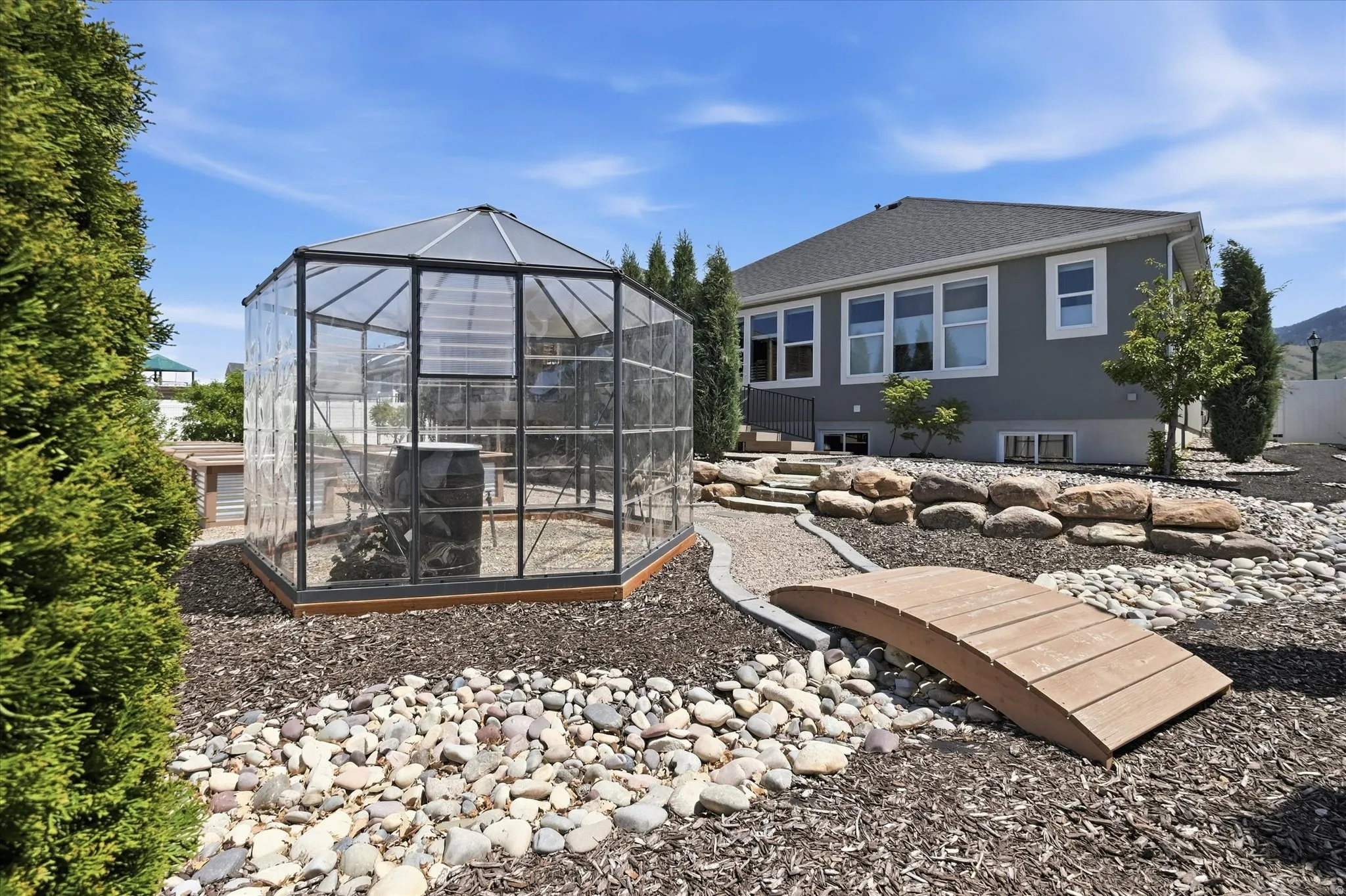 Backyard featuring a hexagonal greenhouse structure, a wooden footbridge, and a rock garden with varied stone sizes