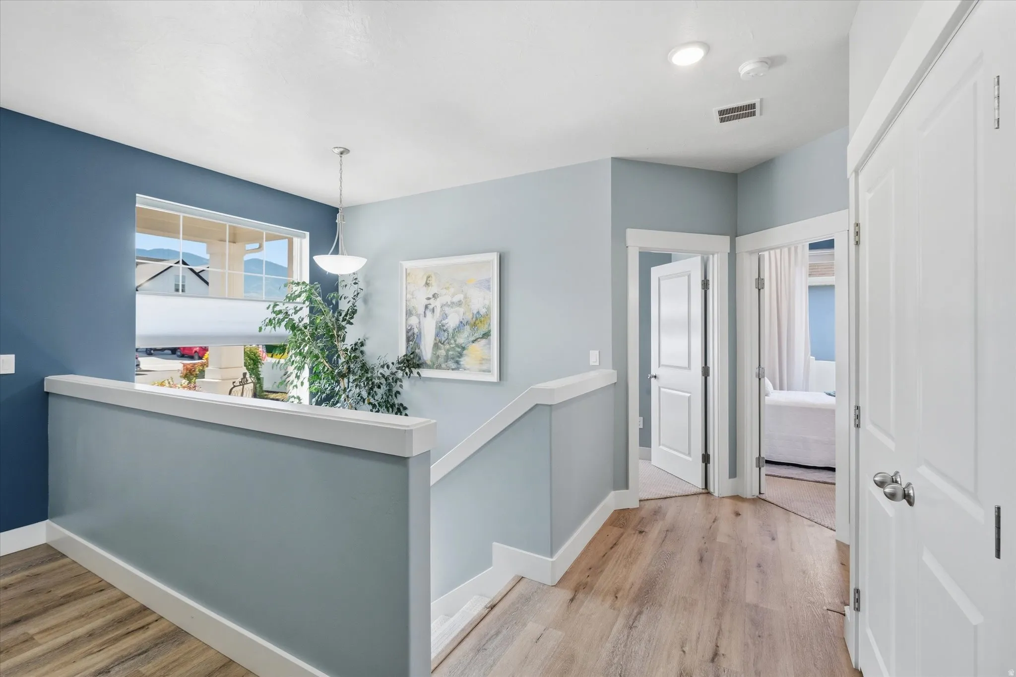 Upper-level landing featuring wood-finish flooring, a window with mountain scenery, a contemporary pendant light fixture, recessed lighting, and multiple paneled doors