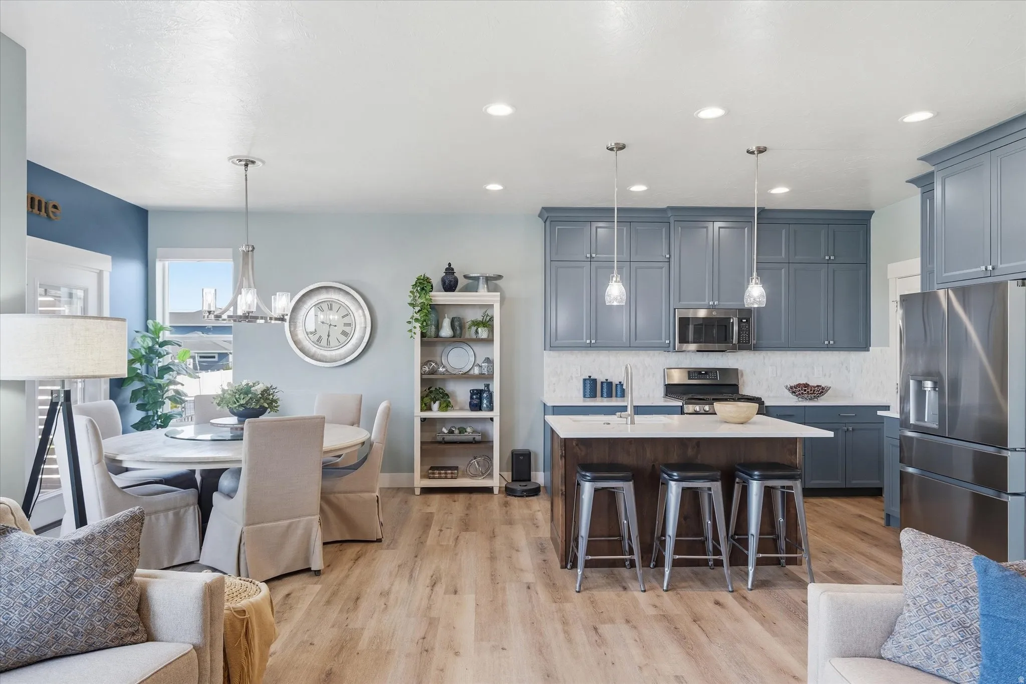 Open-concept living area featuring a kitchen with blue cabinetry and stainless steel appliances, a central island with bar seating, and light wood-finish flooring