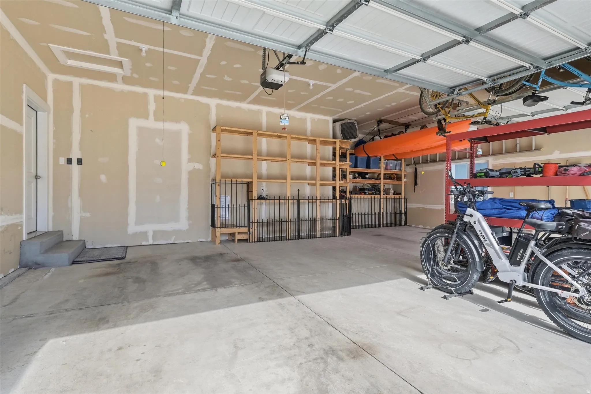 Spacious 3 car garage featuring a concrete floor, overhead door, and ample storage solutions including built-in shelving