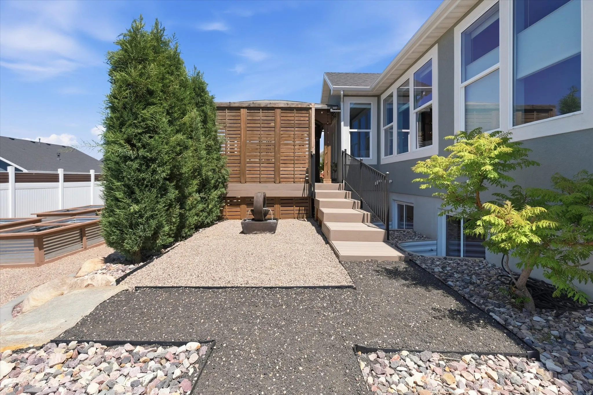 Split-level exterior featuring a ground-level patio with multiple landscaping elements, including gravel paths, decorative rocks, and mature plantings