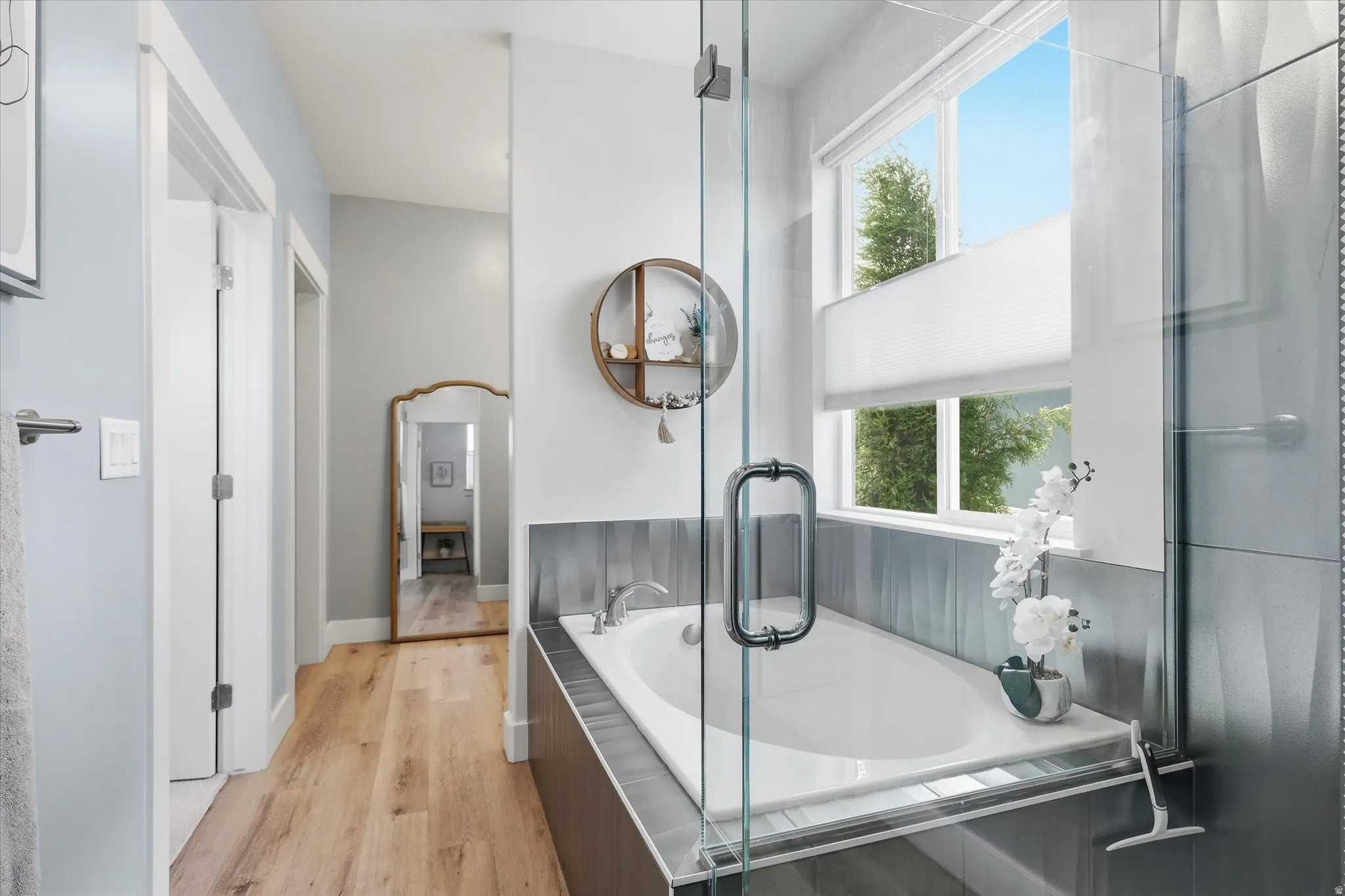 Soaking tub featuring a tiled surround, framed by a large window with privacy blinds