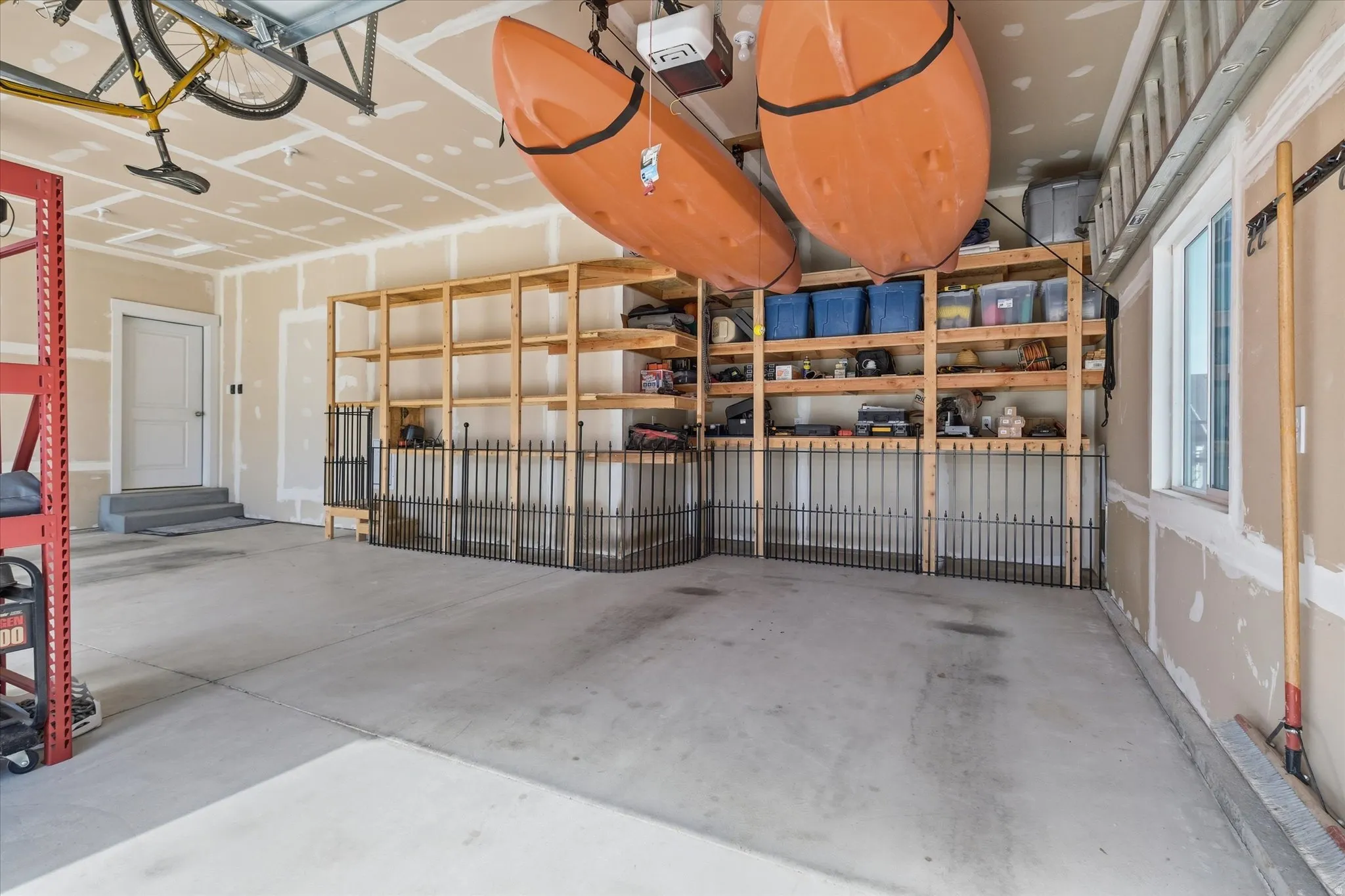 Spacious 3 car garage with concrete flooring, built-in wooden shelving, and a perimeter railing system