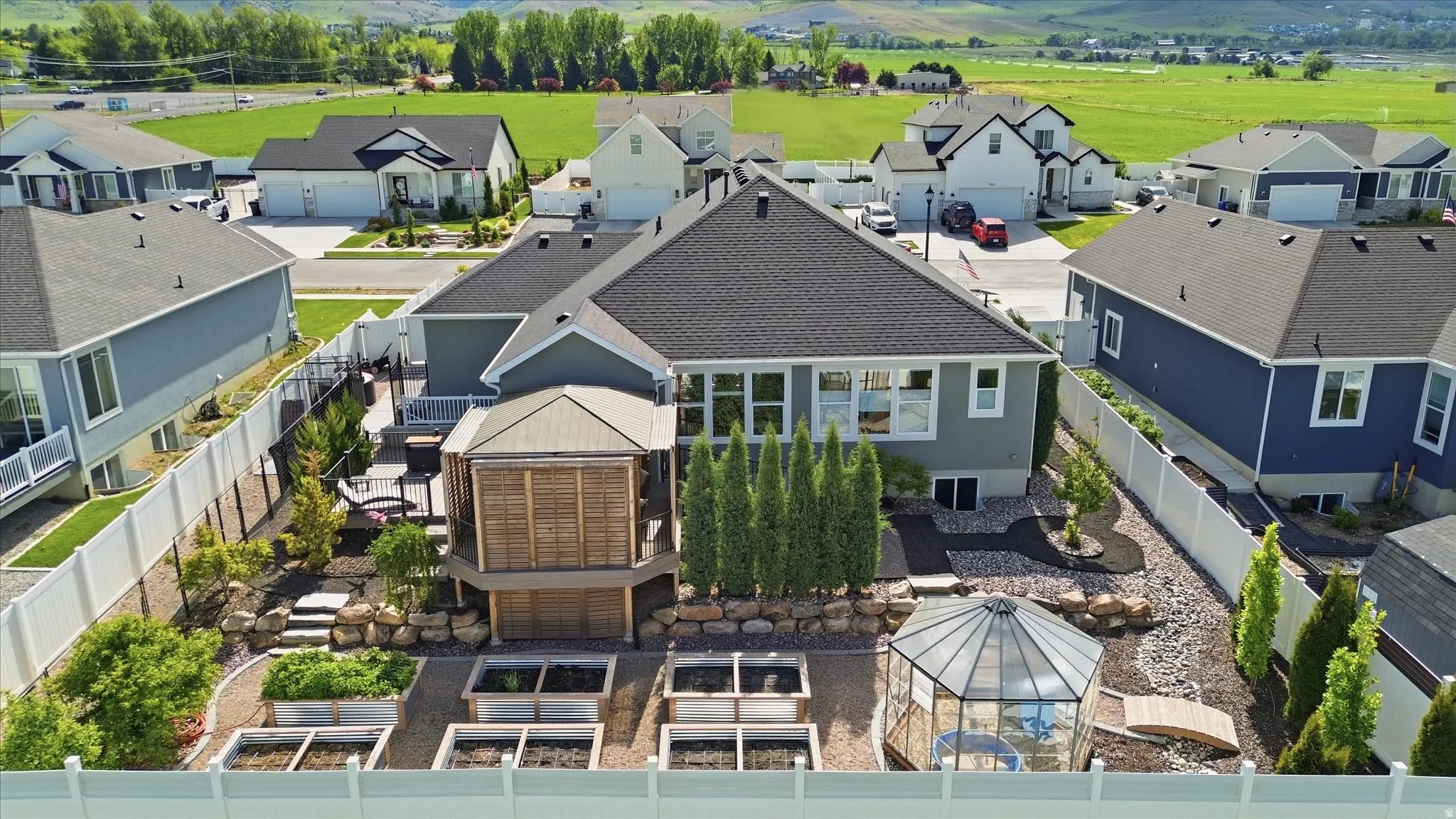 Expansive backyard featuring a multi-level deck with a covered gazebo, numerous raised garden beds, a dedicated greenhouse, and mature landscaping