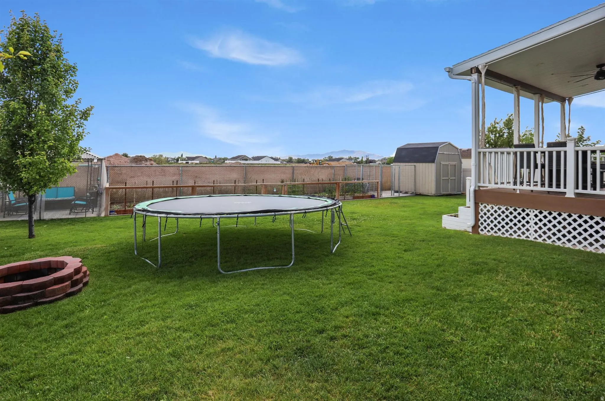 Expansive backyard featuring a manicured lawn, a red brick fire pit, and a covered back patio with white railings