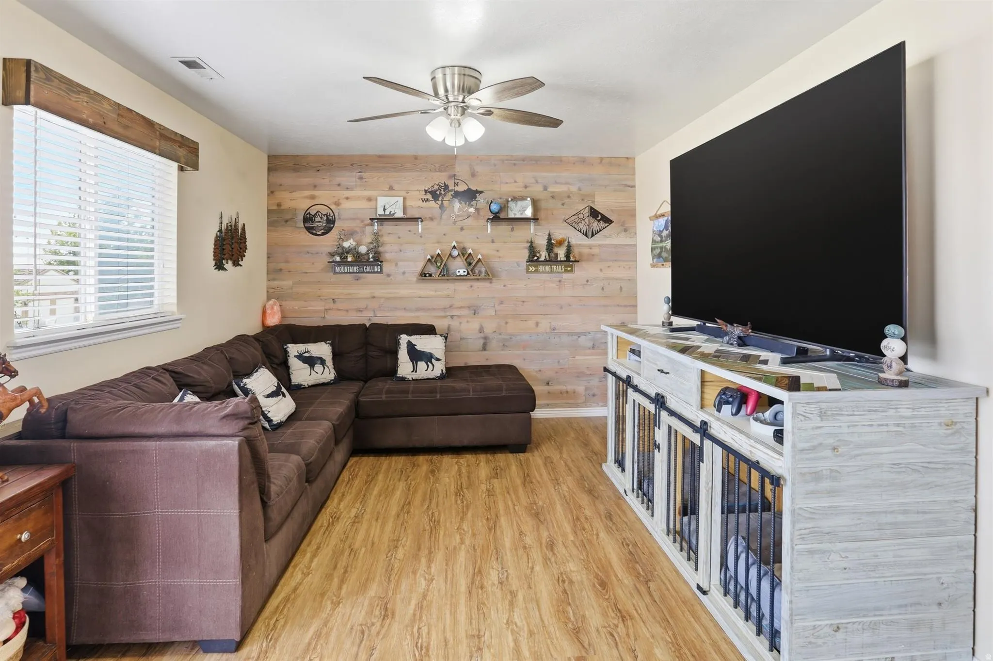 Famiiy room featuring plank wood-finish flooring, a decorative accent wall, and a ceiling fan with integrated lighting