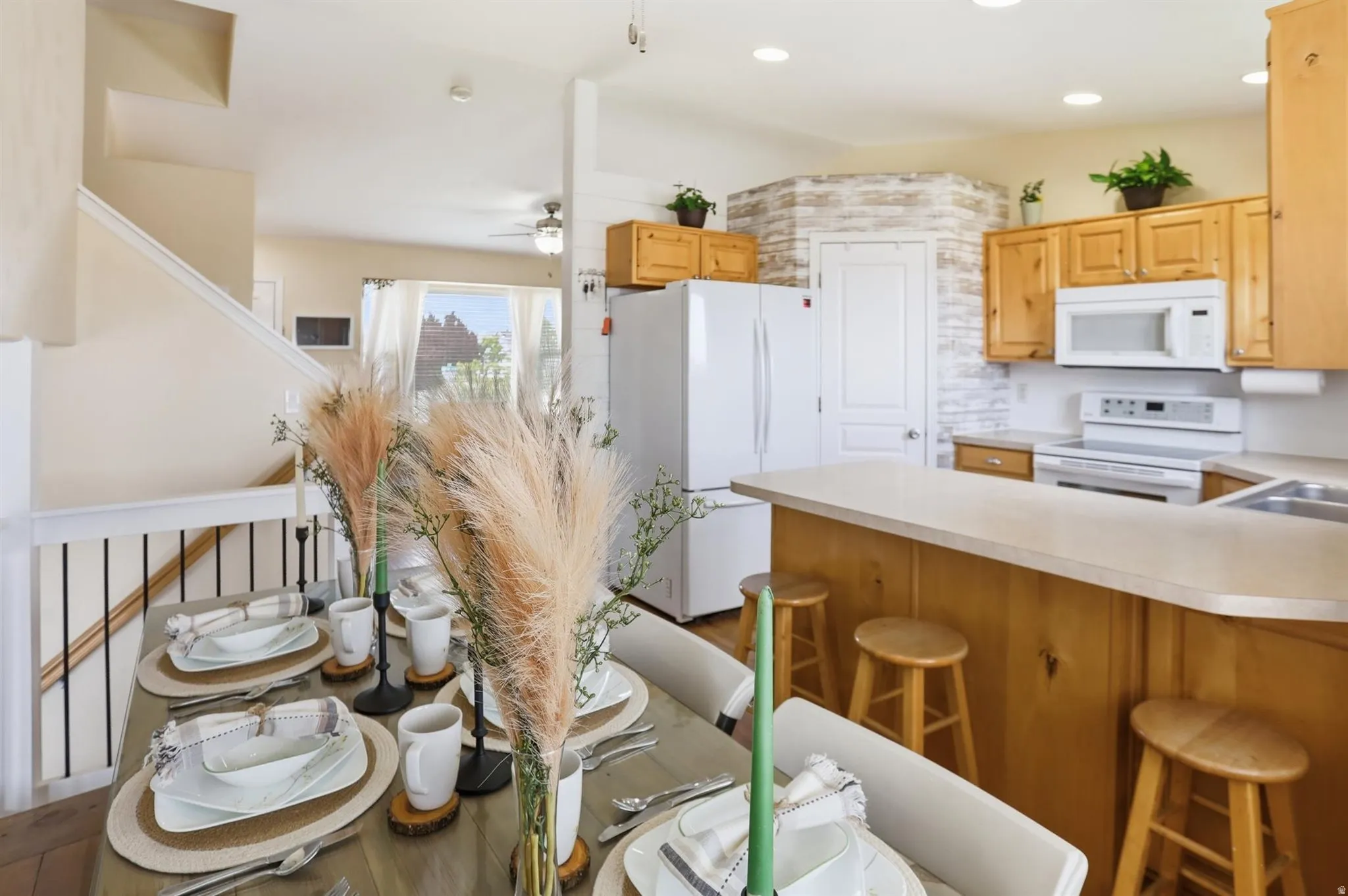 Open-concept kitchen and dining area featuring light wood cabinetry, white appliances, a breakfast bar, and a light-toned countertop