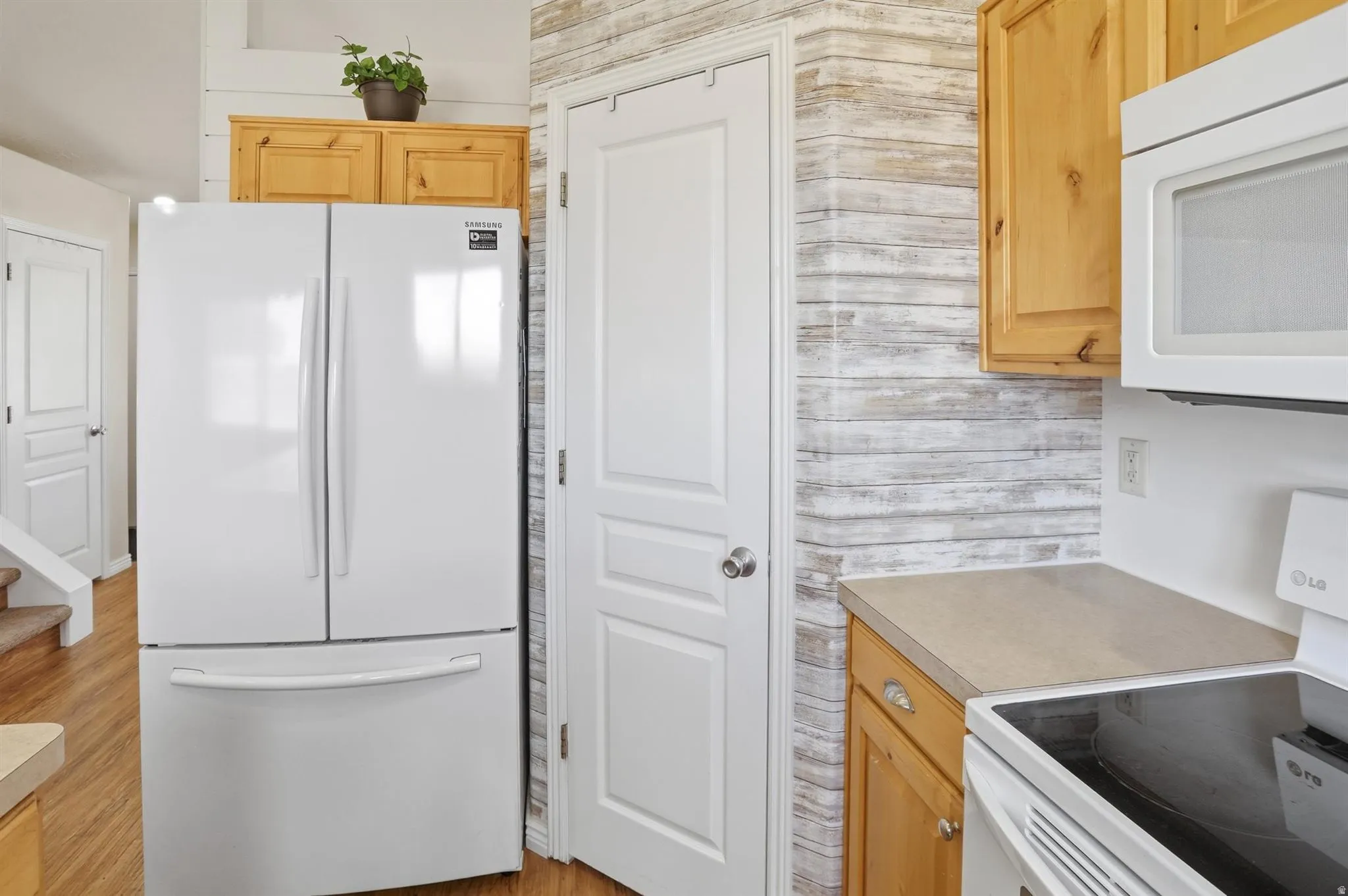 Kitchen featuring light wood cabinetry, stone-finish countertops, and a white refrigerator, pantry