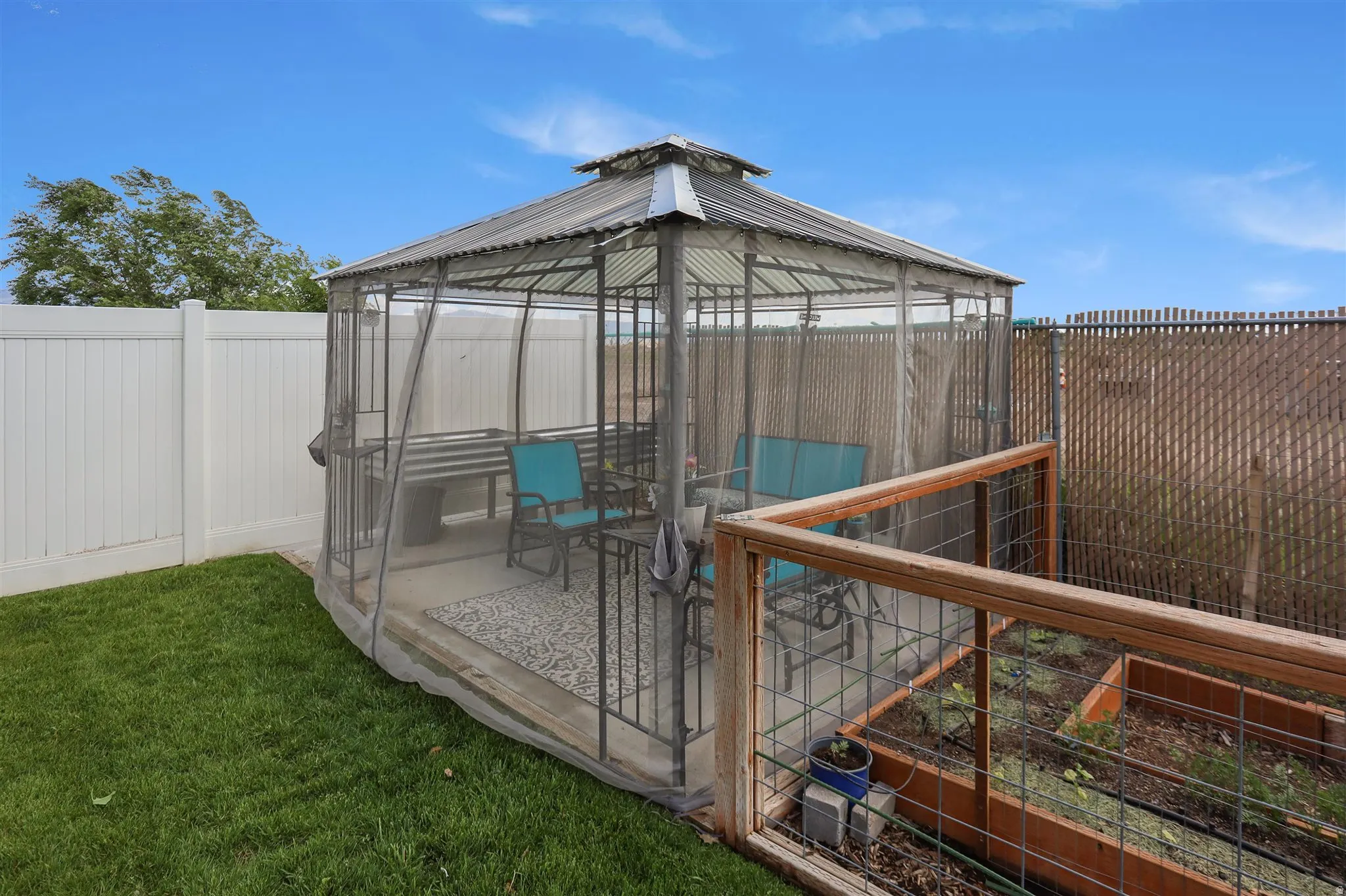 Screened gazebo with a corrugated metal roof, concrete patio base, and surrounding manicured lawn