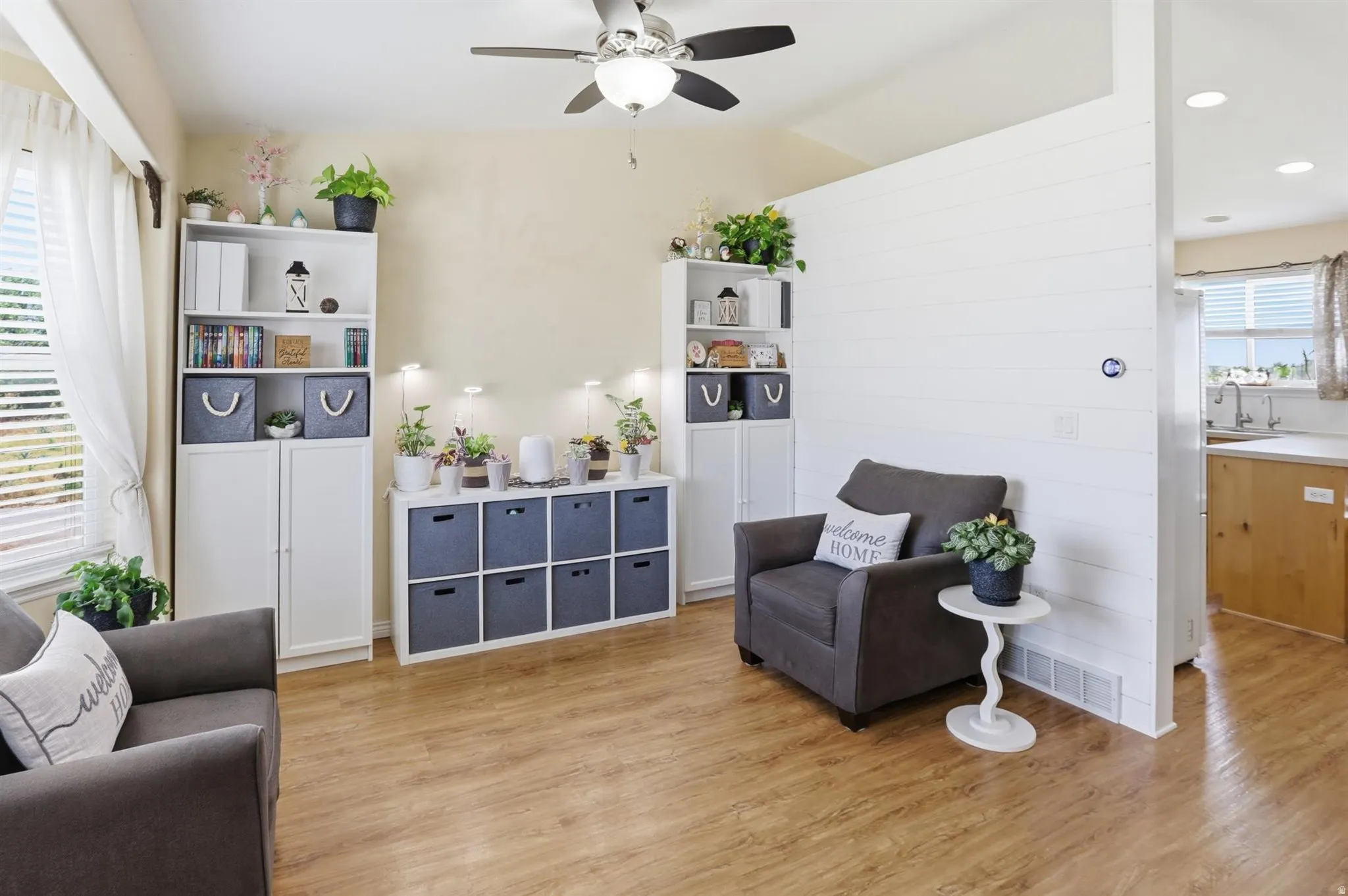 Spacious living area featuring wood-finish flooring, a ceiling fan, and a partial shiplap wall