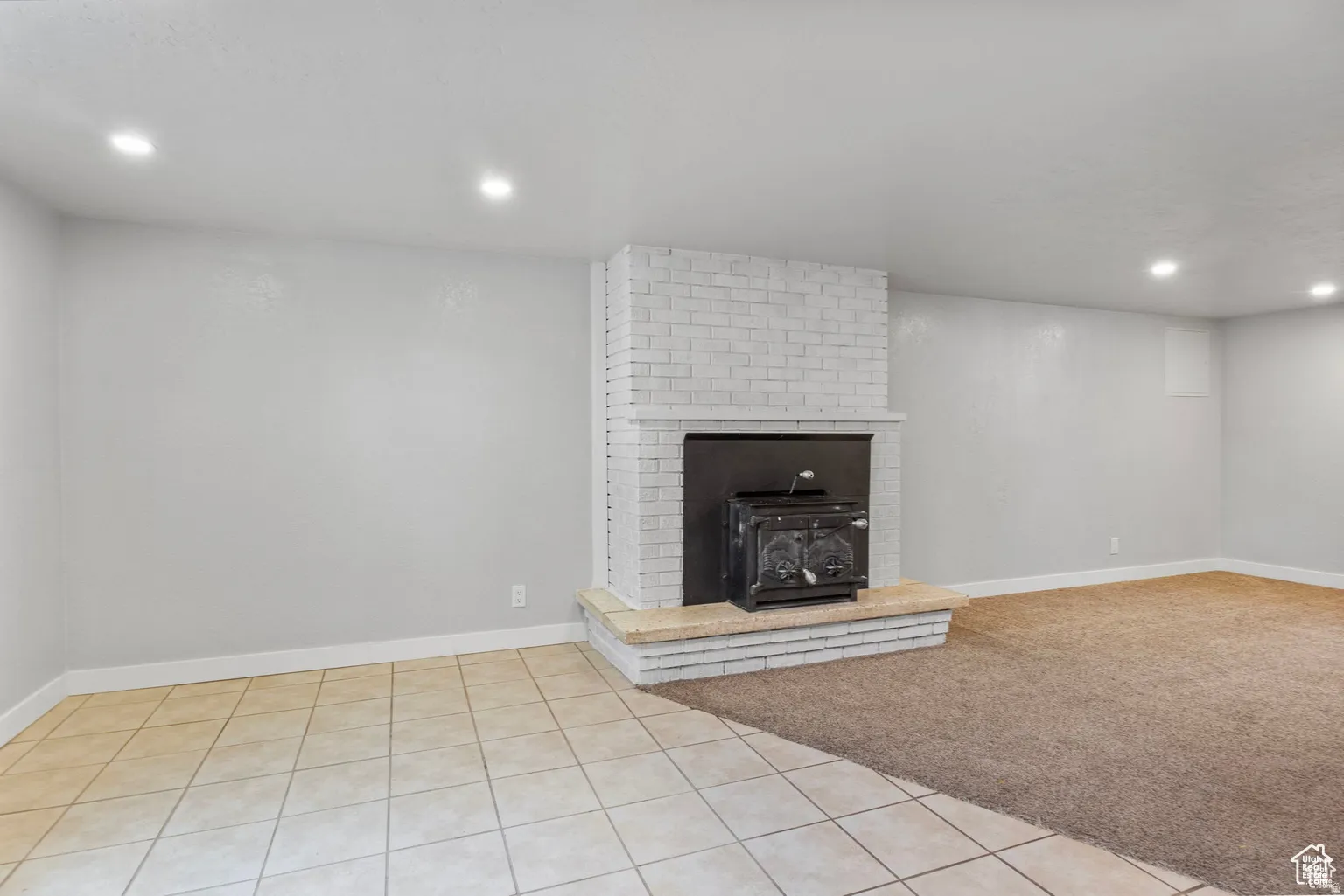 Brick fireplace with wood-burning stove and mantel, recessed lighting, and mixed flooring featuring tile and carpet