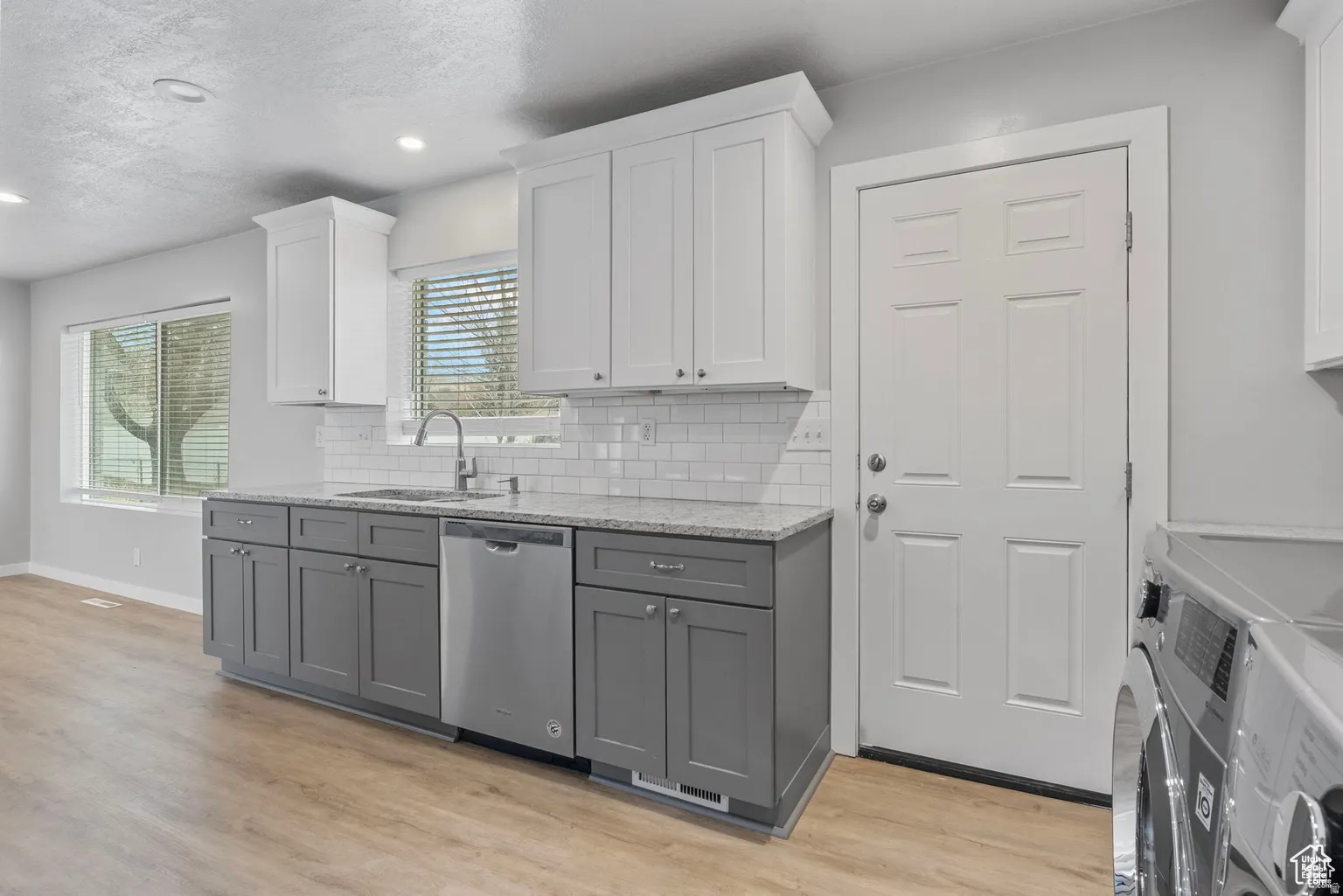 Kitchen area featuring two-tone cabinetry, a stainless steel dishwasher, and a subway tile backsplash