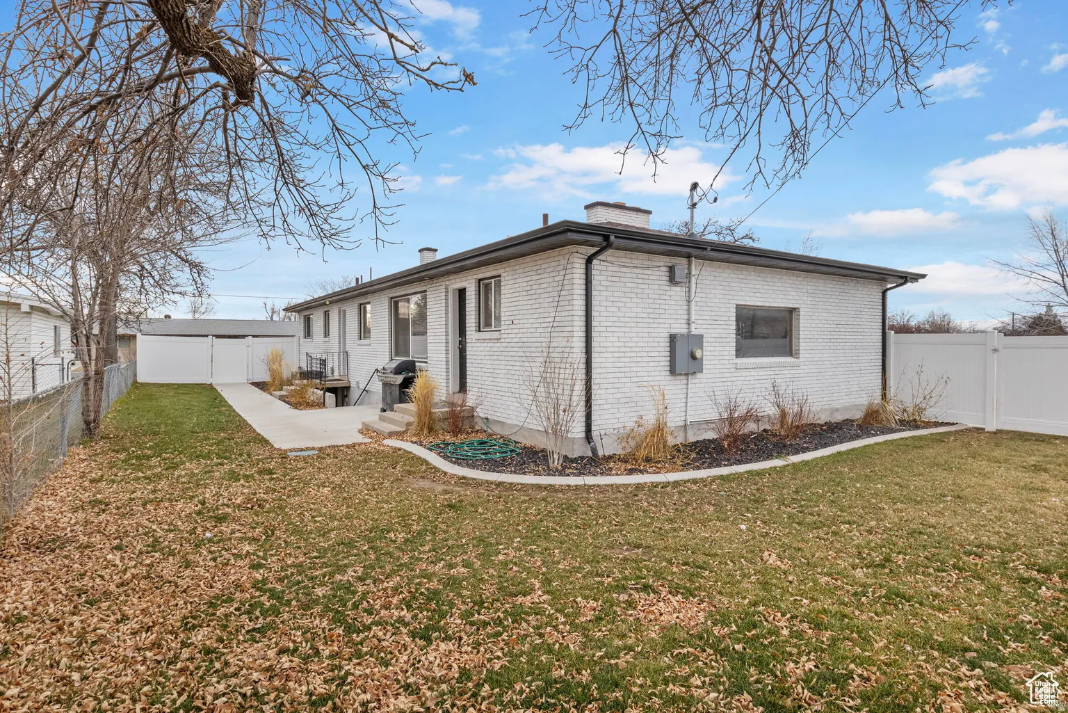 Rear exterior featuring white painted brick, a concrete patio, a manicured lawn, and a white vinyl privacy fence