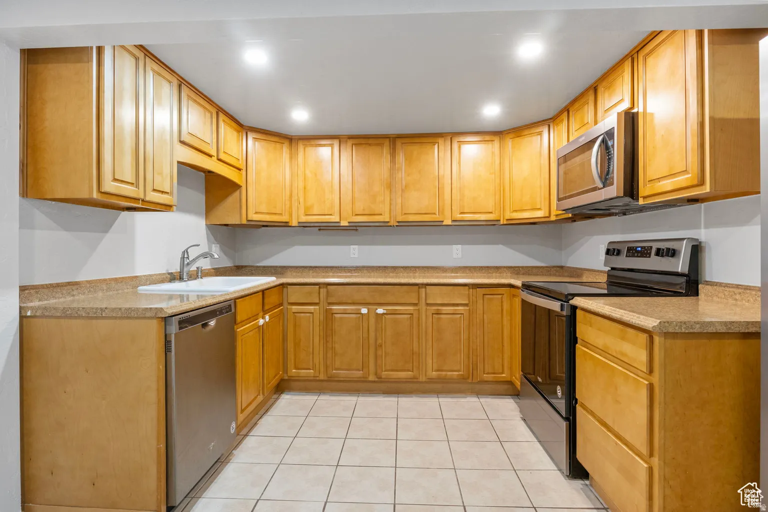 U-shaped kitchen featuring wood-finish cabinetry, light-toned countertops, and recessed lighting