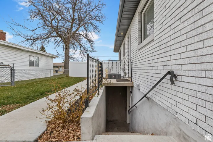 Side exterior featuring white brick siding and a basement entrance with a black metal handrail