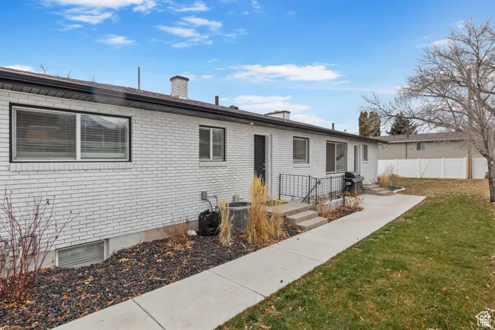 White brick exterior with multiple windows, a concrete walkway, a grassy yard, and mature tree