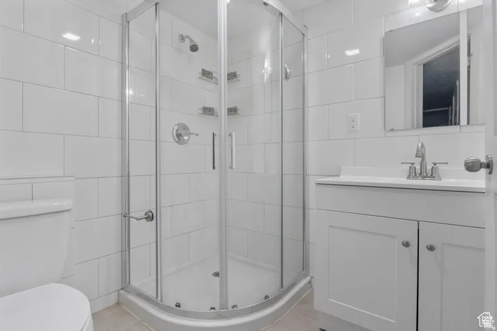Bathroom featuring a curved glass shower enclosure, white subway tile walls, a toilet, a single-sink vanity with a white countertop, and a wall-mounted mirror