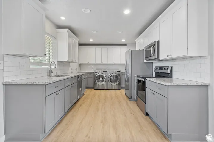 Kitchen featuring two-tone cabinetry, white subway tile backsplash, light-toned wood-finish flooring, and stainless steel appliances