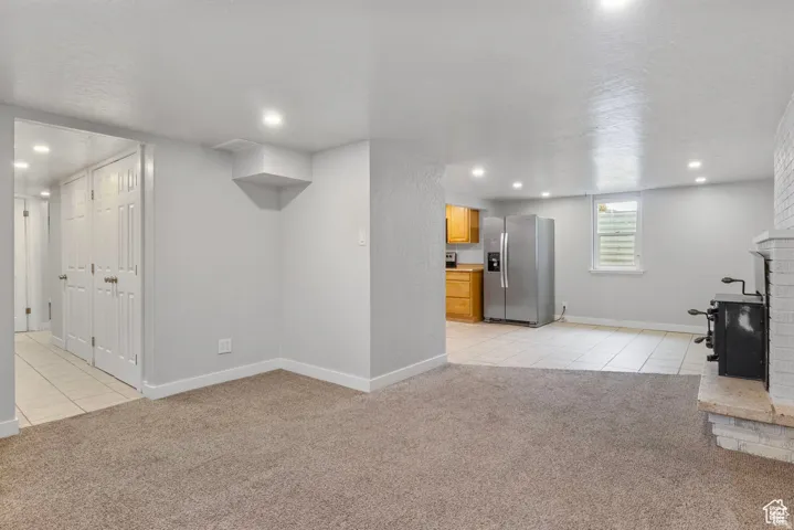 Spacious room with plush carpet flooring, recessed lighting, and a white brick fireplace featuring a black wood-burning stove