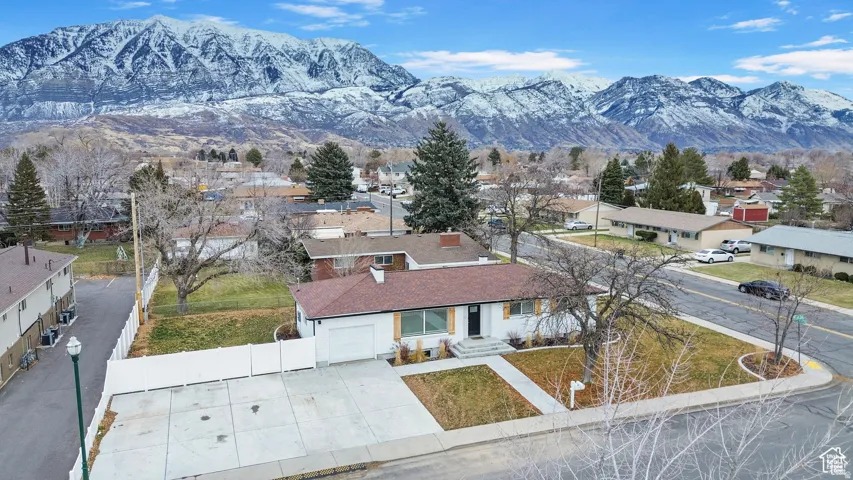 Corner lot property featuring a white exterior with dark brown shutters, an attached garage, and a concrete driveway