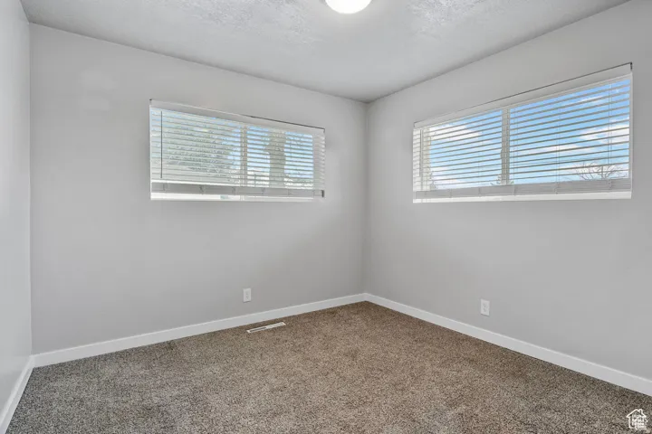 Room featuring two windows with white horizontal blinds, light gray wall paint, white baseboards, and gray speckled carpet flooring