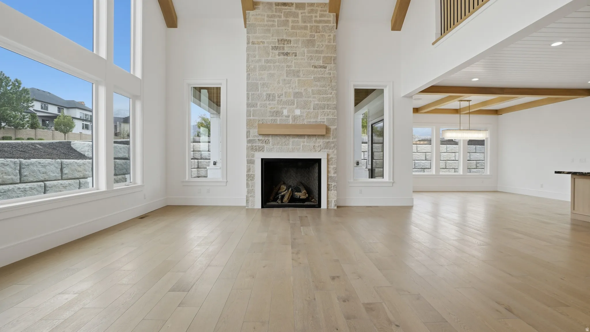 Two-story living area featuring a stacked stone fireplace with a wood mantel, light wood-finish flooring, and expansive windows