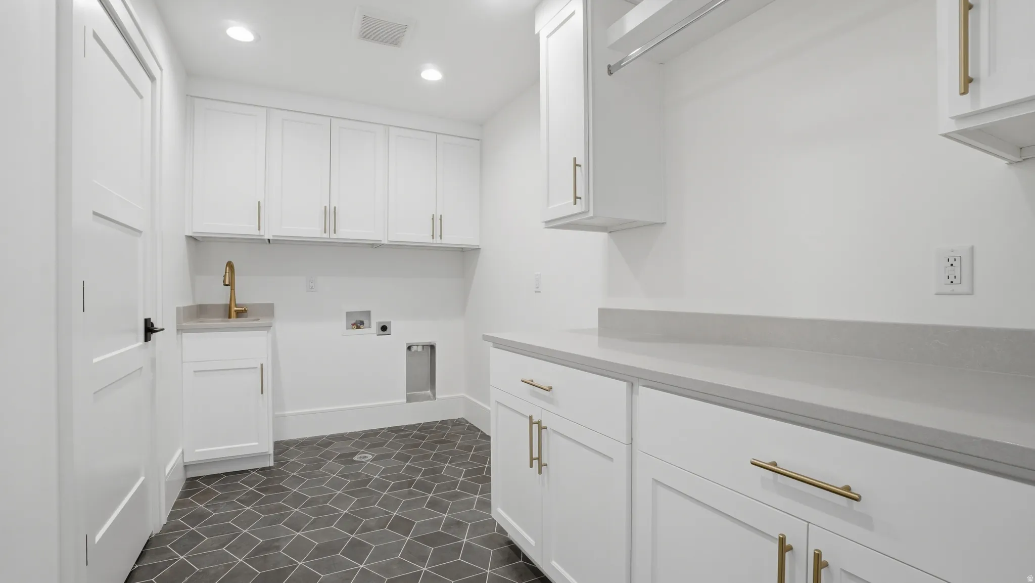 Dedicated laundry space featuring white shaker cabinetry, an integrated sink with a gold-finish faucet, and substantial countertop space