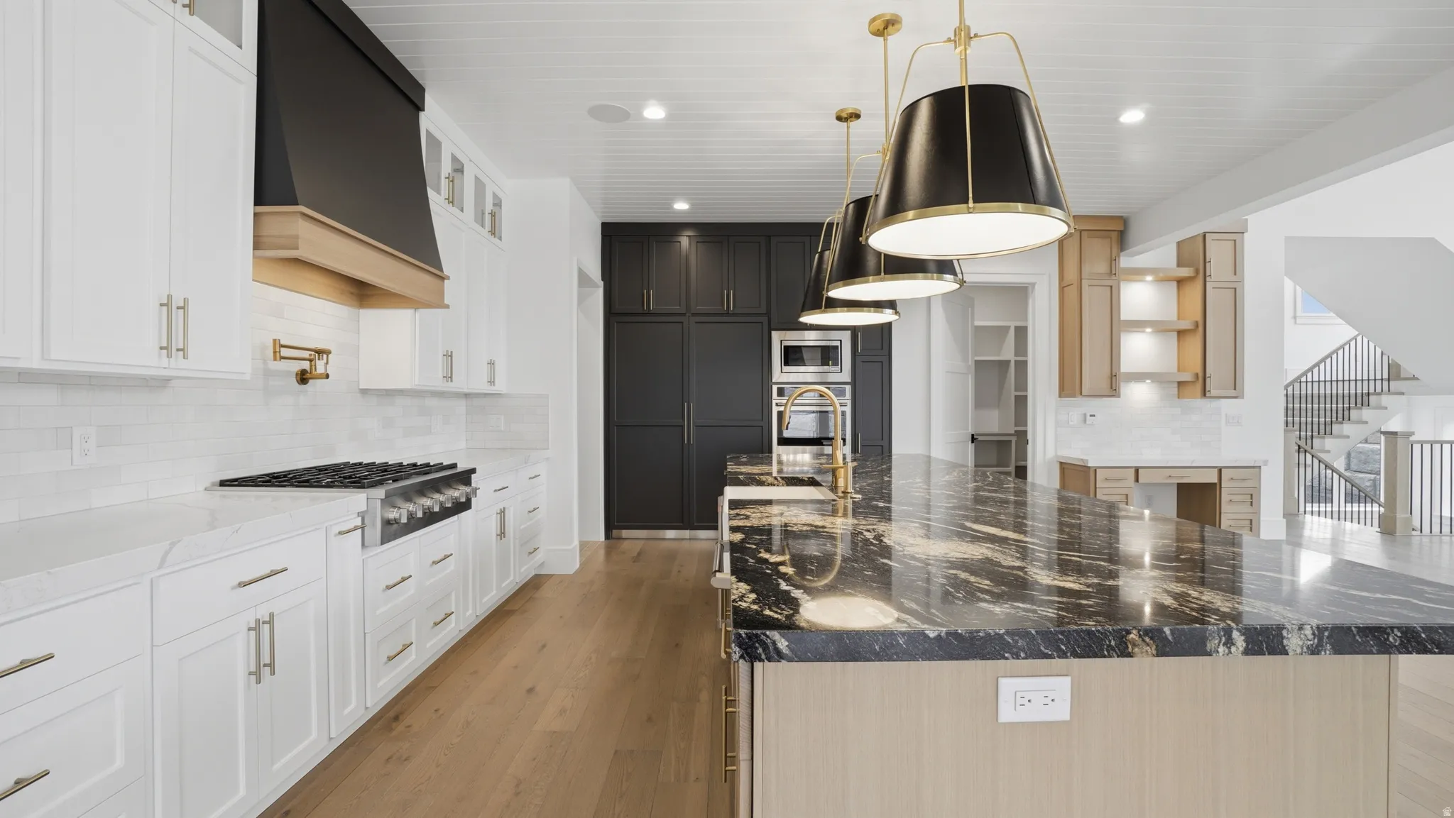 Kitchen featuring a large island with a patterned countertop, white perimeter cabinetry, a stainless steel range with a pot filler faucet, and wood-finish flooring