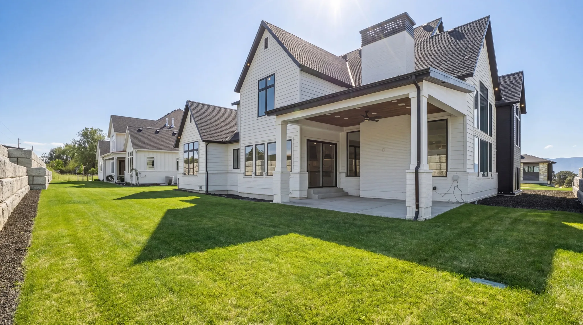 Expansive rear facade featuring white siding, black-framed windows, and a covered patio with a ceiling fan