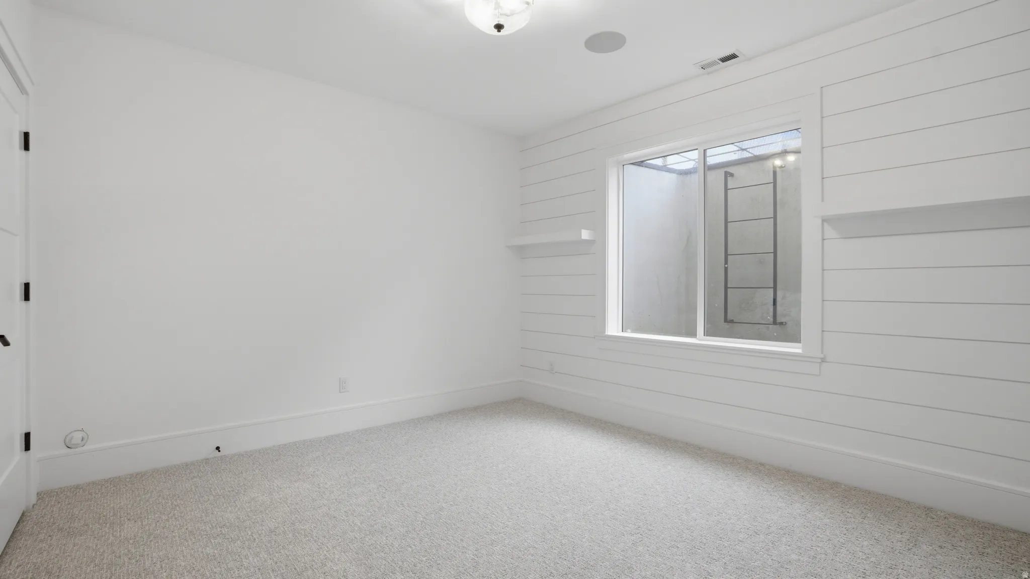 Room featuring shiplap accent wall with integrated shelving, window with exterior ladder, recessed ceiling speaker, and light-toned carpet flooring