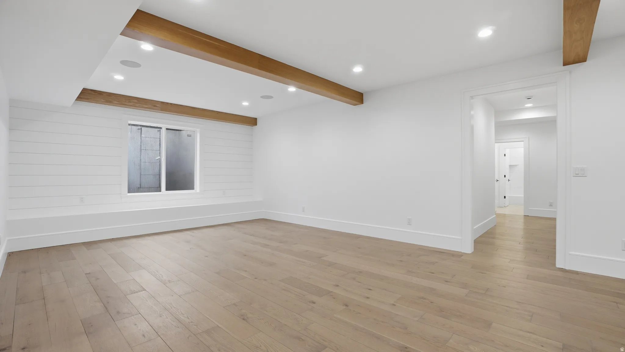 Spacious room featuring wood-finish flooring, recessed lighting, and exposed ceiling beams