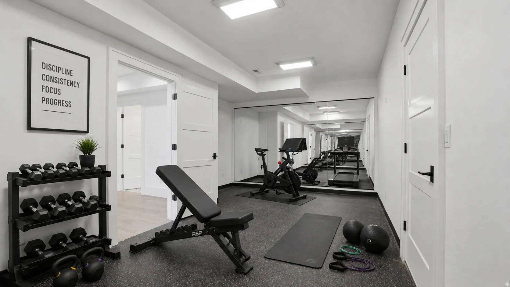 Dedicated fitness room featuring resilient rubber flooring, expansive wall-mounted mirrors, recessed lighting, and contemporary white doors with dark hardware