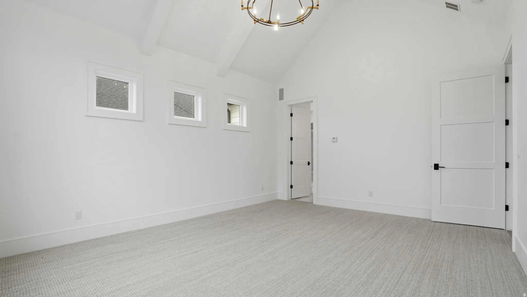 Spacious room featuring vaulted ceilings with exposed beams, light-colored carpeting, multiple windows, and a modern chandelier
