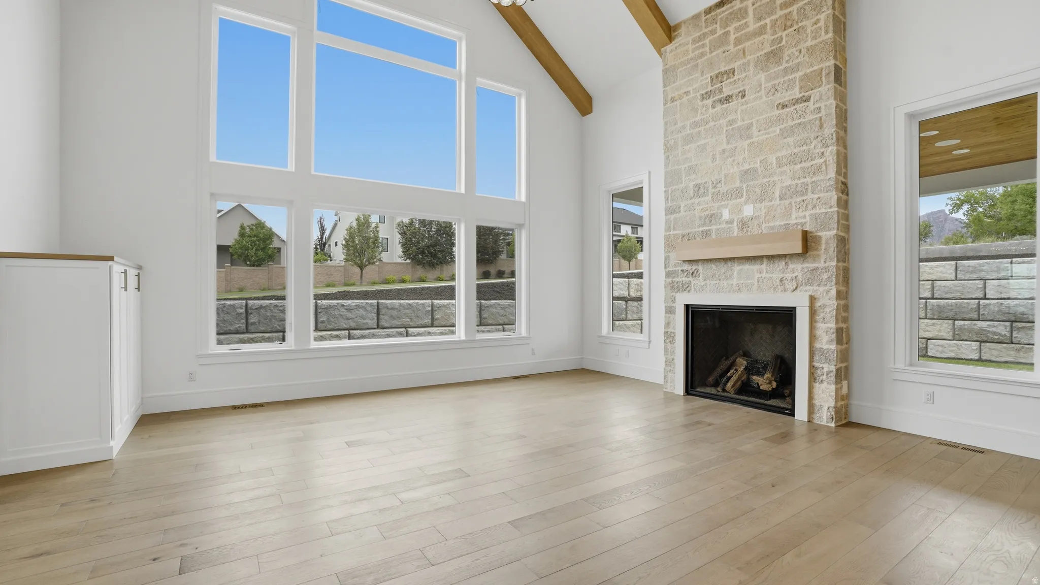 Vaulted living space featuring a floor-to-ceiling stone fireplace with a wood mantle, wood-finish flooring, exposed ceiling beams, and a built-in cabinet with a wood countertop