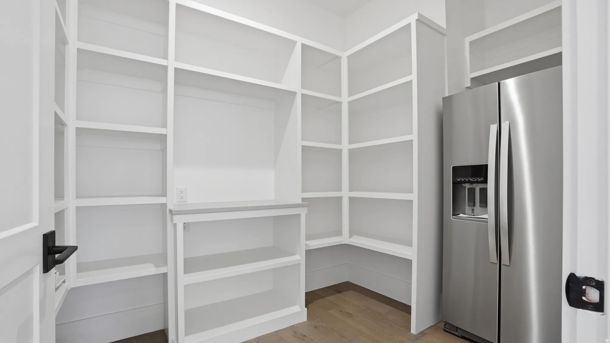 Walk-in pantry featuring extensive built-in shelving, a built-in counter, and wood-finish flooring