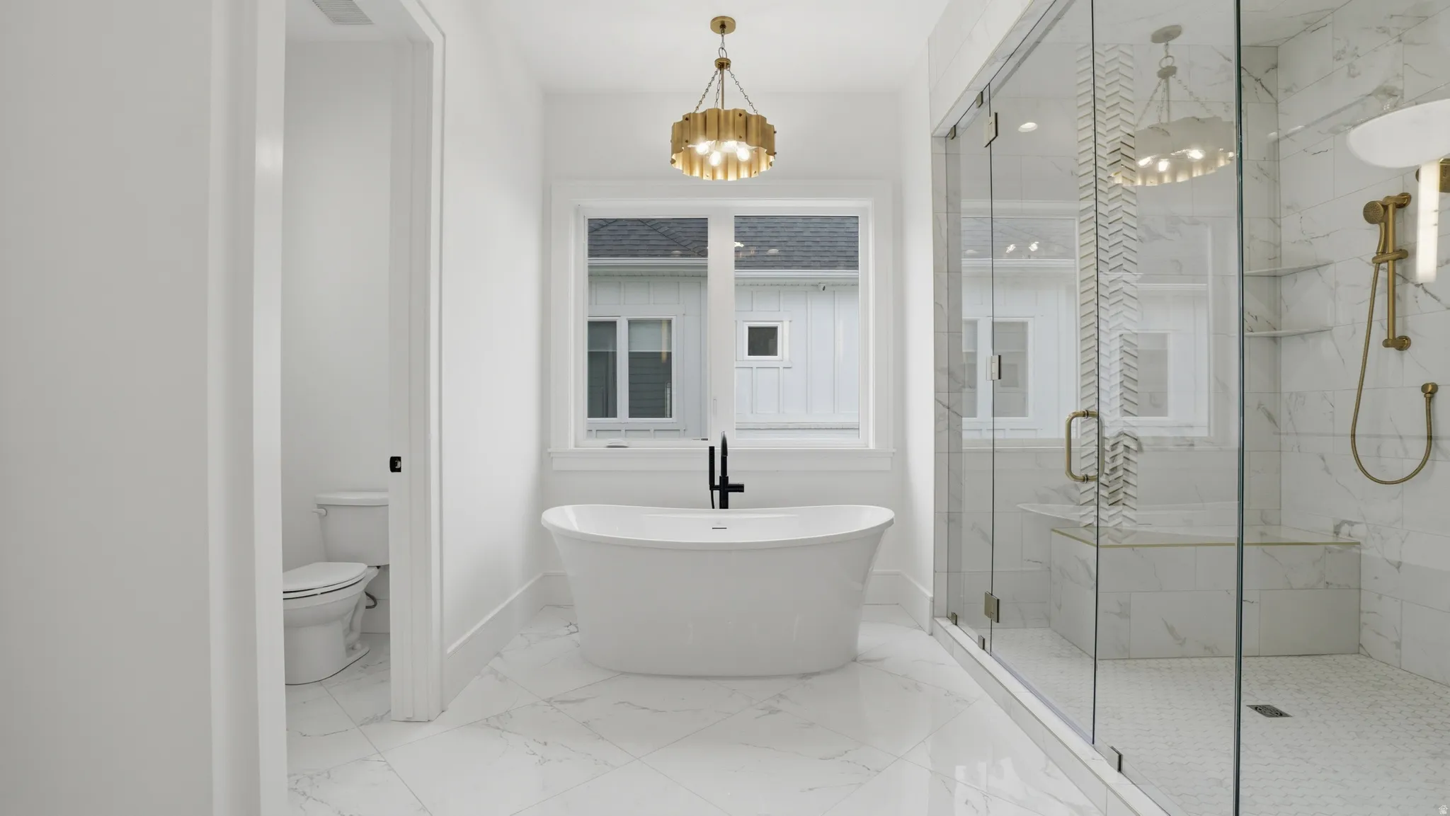 Freestanding bathtub with a black wall-mounted faucet, complemented by a gold-finish chandelier