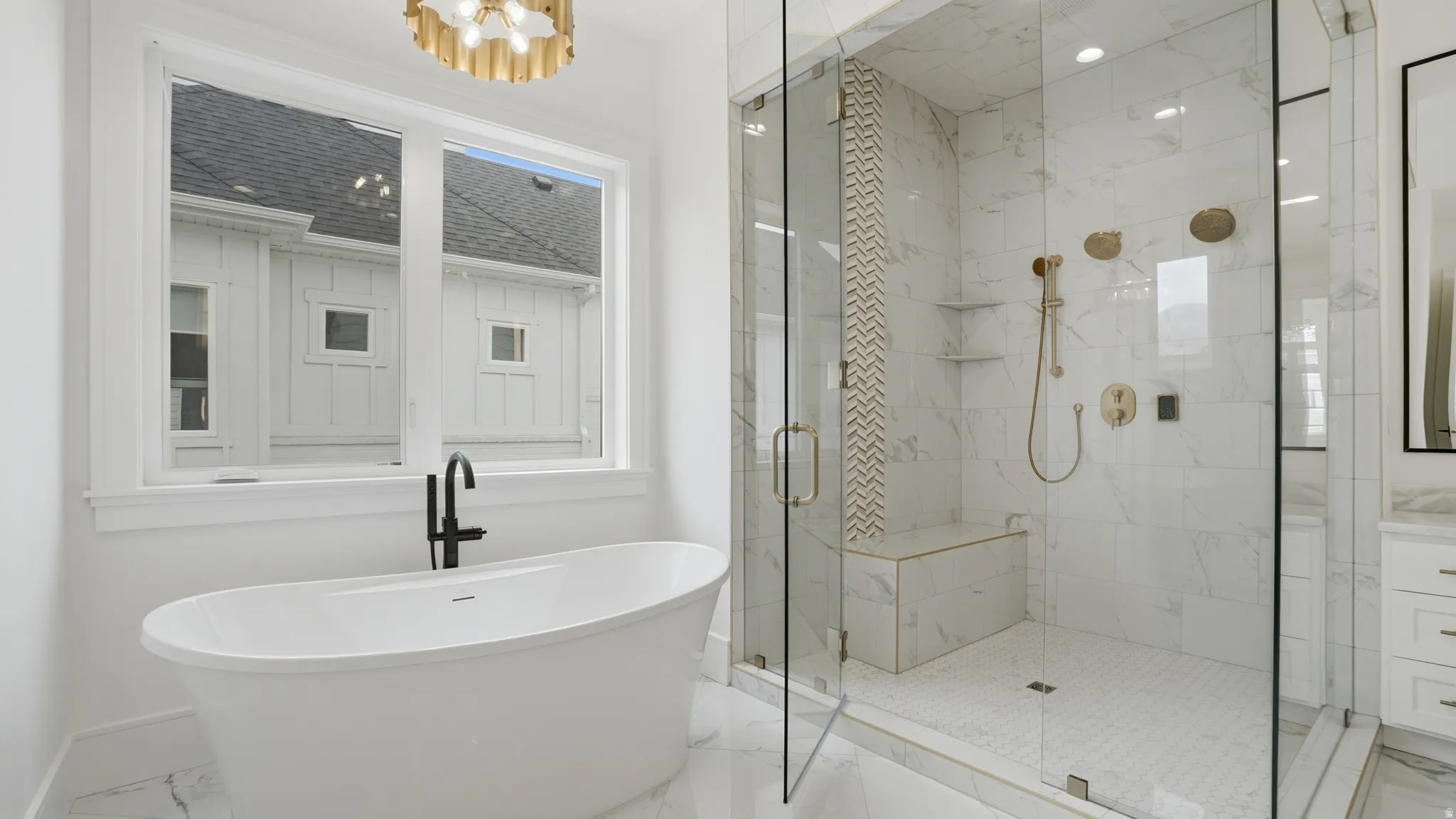 Freestanding soaking tub with a matte black faucet, full glass shower enclosure with a built-in bench, marble-finish tile, and brass shower fixtures