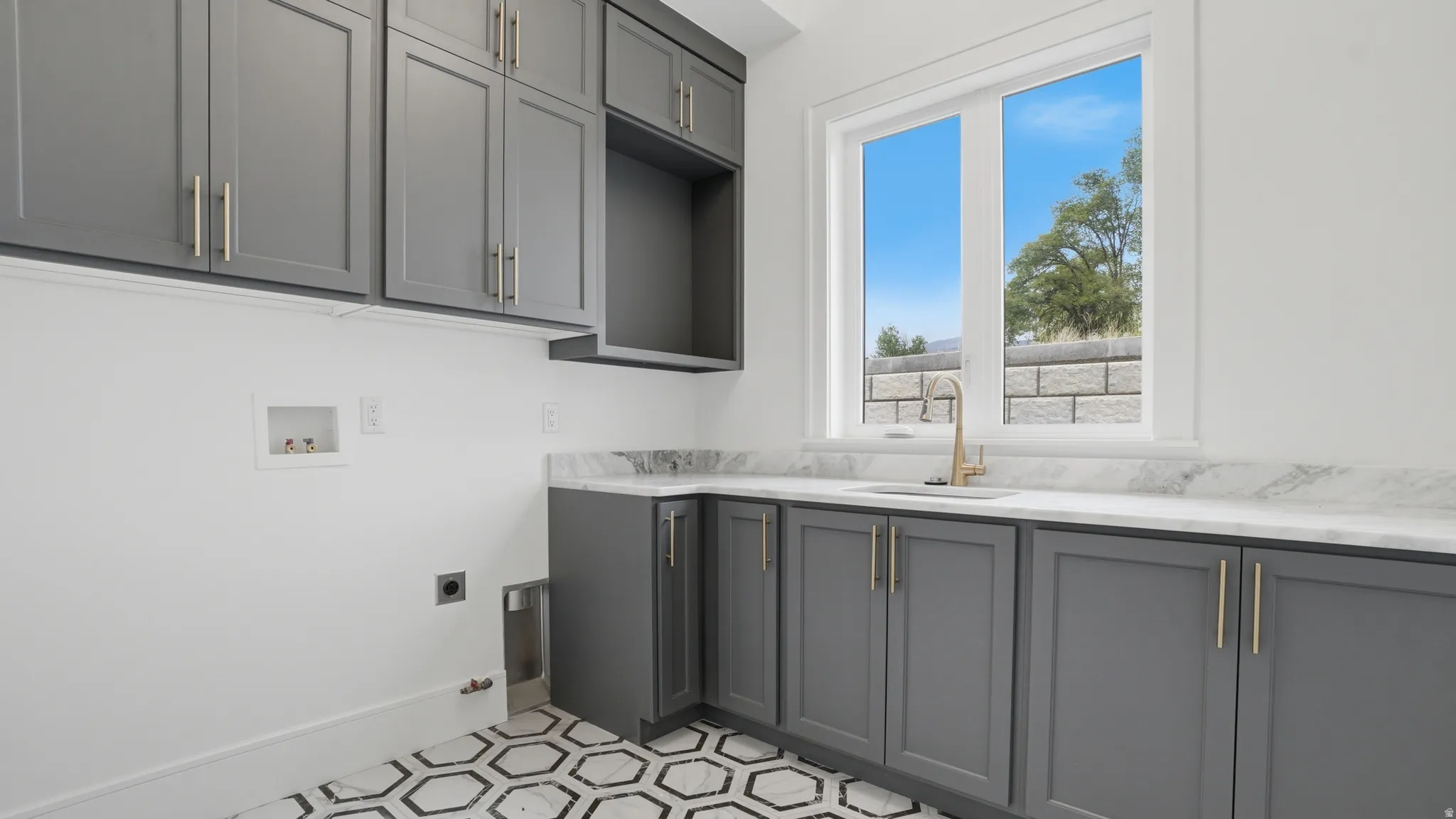 Laundry room featuring gray cabinetry, a white countertop, an undermount sink with a gold-tone faucet, and hexagonal floor tiling
