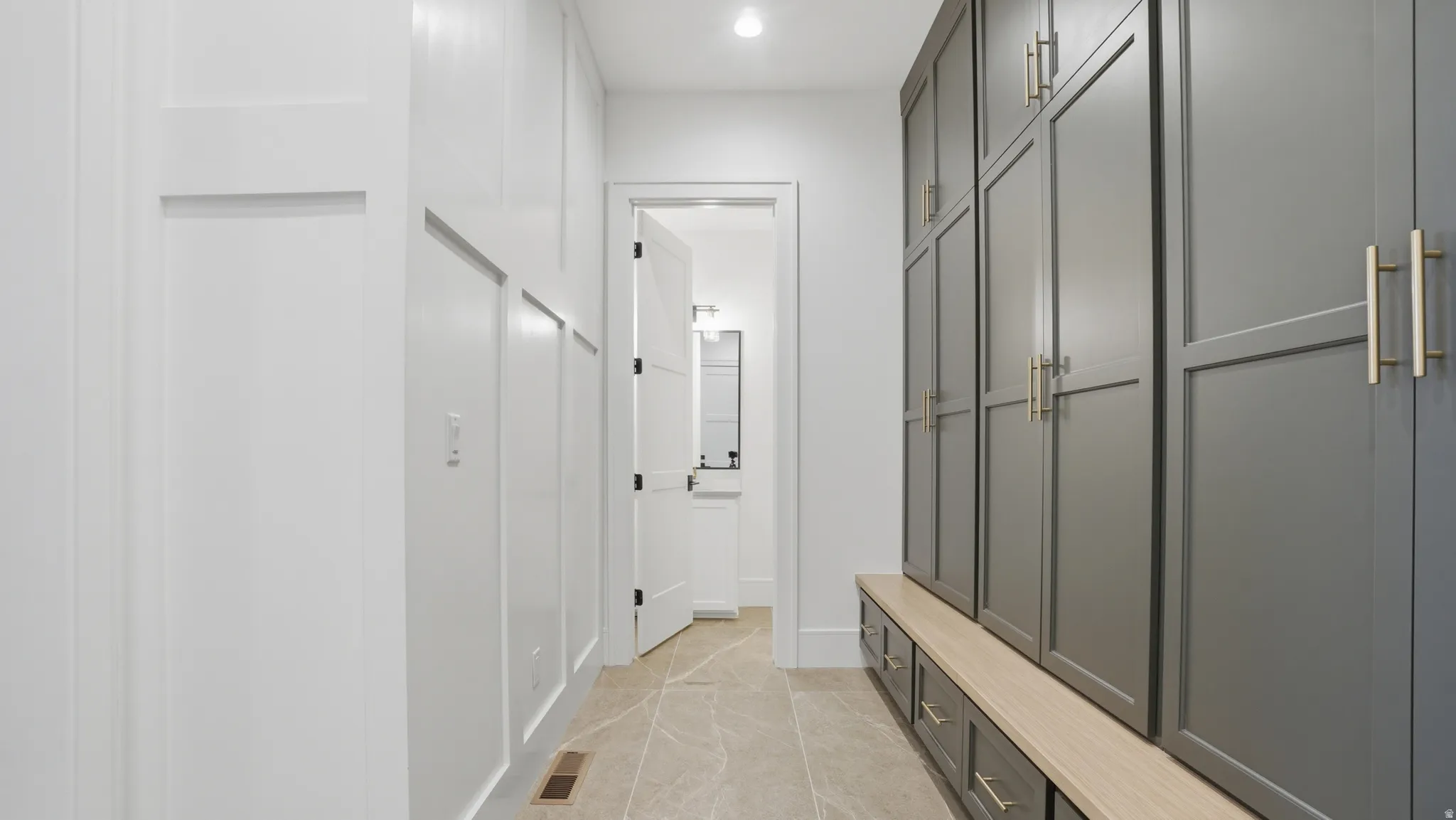 Hallway featuring board-and-batten wall detailing, large format tile flooring, built-in cabinetry with gold-toned hardware, and an integrated bench with storage drawers
