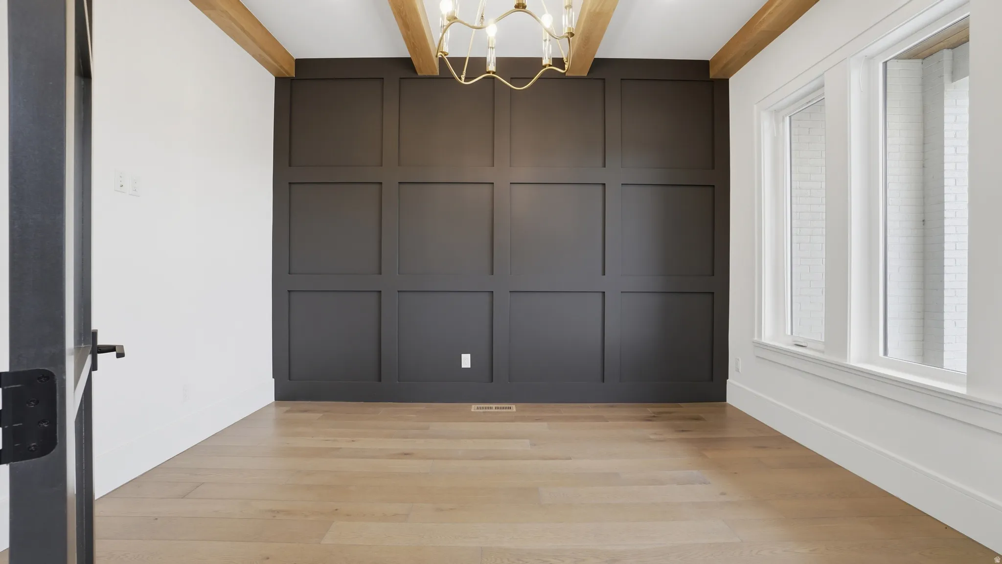Room featuring wood-finish flooring, a paneled accent wall, exposed ceiling beams, and a brass chandelier