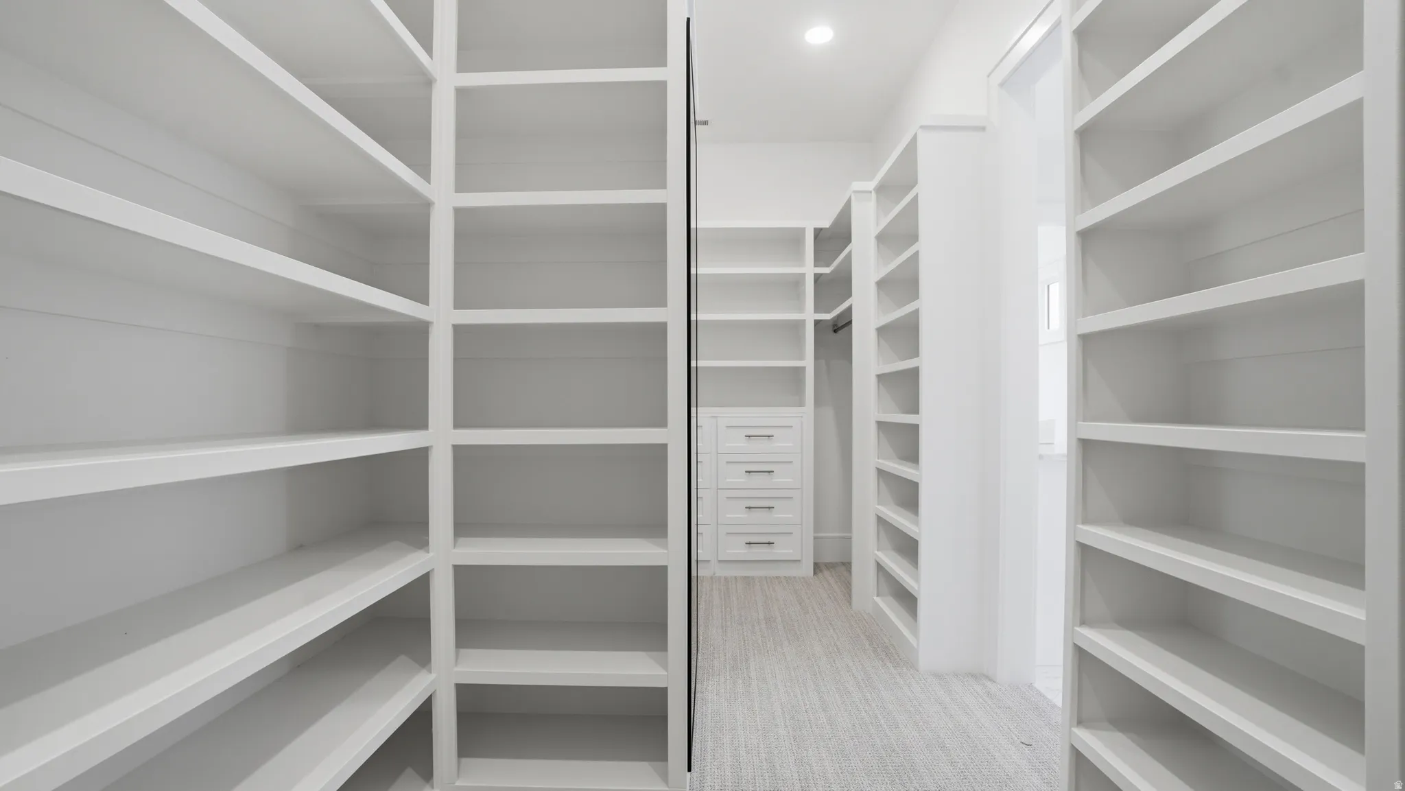Expansive walk-in closet featuring built-in shelving, integrated drawer storage, a hanging rod, recessed lighting, and light-toned flooring