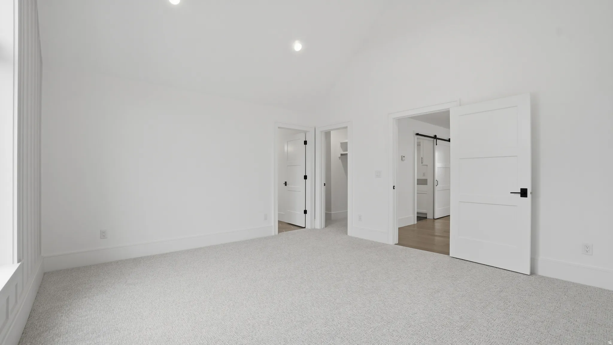 Spacious room featuring vaulted ceilings, light-colored carpet, recessed lighting, and white trim