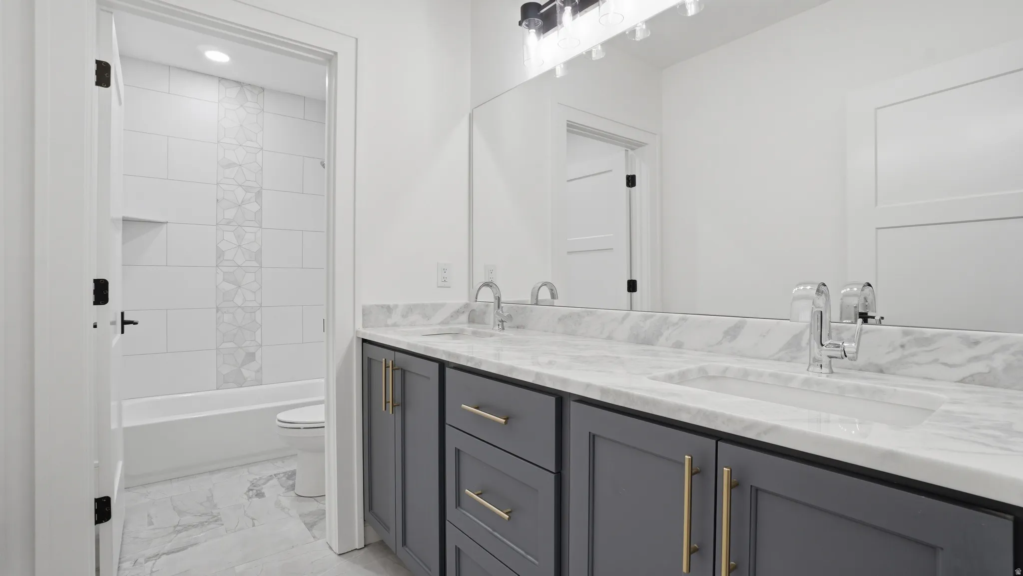Double vanity with marble-finish countertop and integrated sinks, featuring gray cabinetry with gold-tone hardware