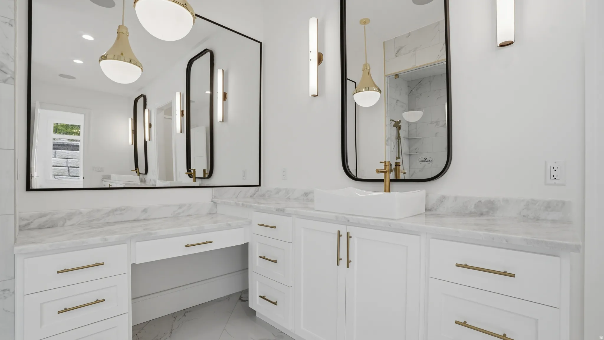 Bathroom vanity featuring white cabinetry with brass hardware, a contrasting white vessel sink, and a large wall-mounted mirror