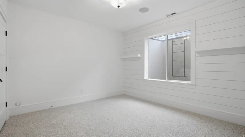 Room featuring shiplap accent wall with integrated shelving, window with exterior ladder, recessed ceiling speaker, and light-toned carpet flooring