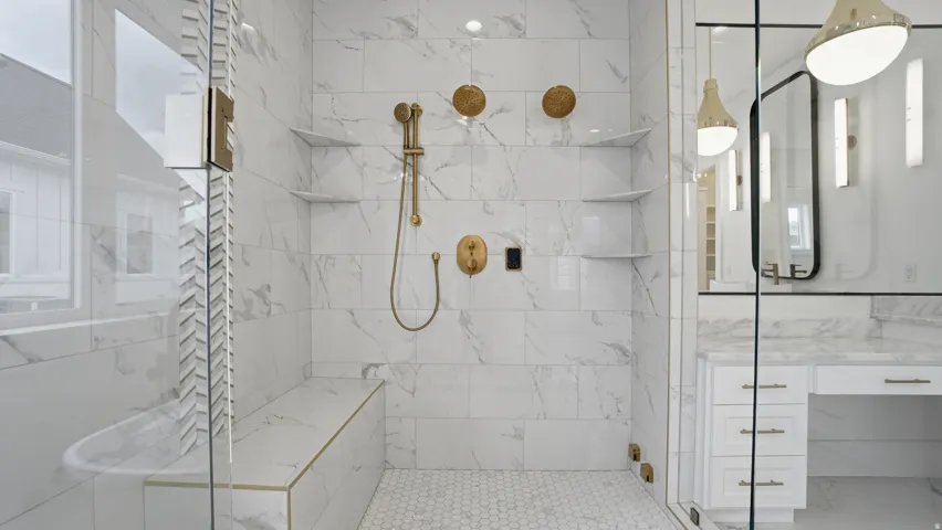 Walk-in shower with full height stone-look tile, hexagonal floor tile, built-in bench with gold-tone trim, and built-in shelving