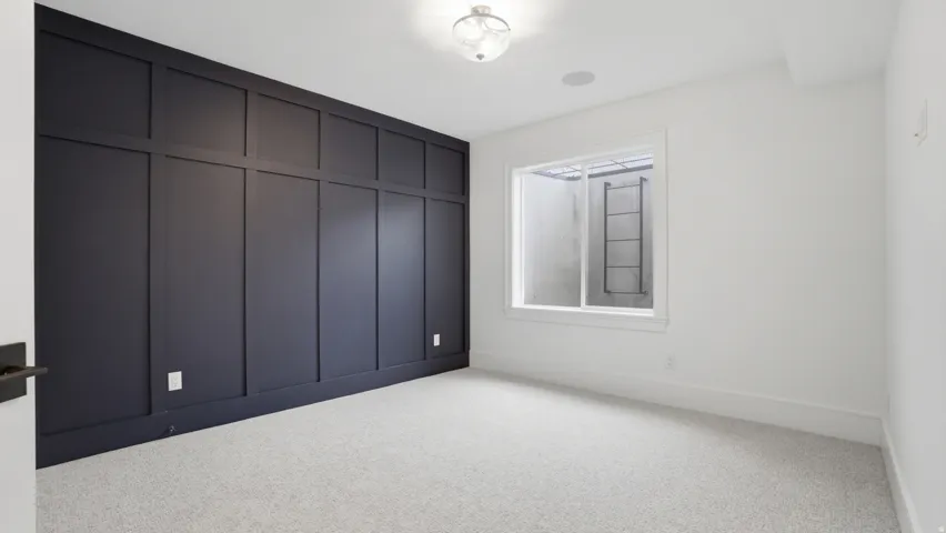 Accent wall with dark wainscoting and trim, light gray textured carpet, recessed ceiling speaker, ceiling-mounted light fixture, and white window trim