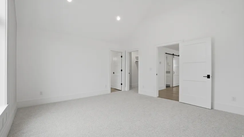 Spacious room featuring vaulted ceilings, light-colored carpet, recessed lighting, and white trim