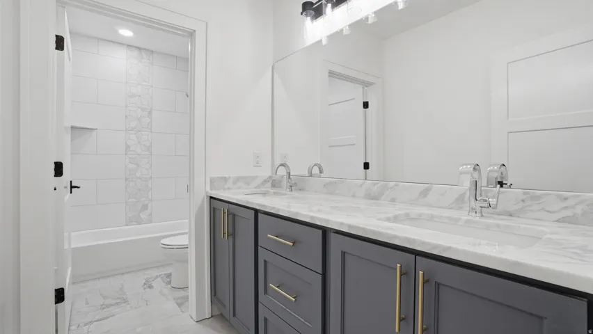 Double vanity with marble-finish countertop and integrated sinks, featuring gray cabinetry with gold-tone hardware